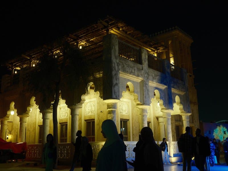 Illuminated historical building at night with silhouettes of people in the foreground.