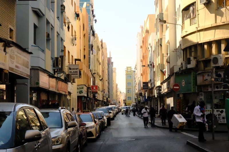 A bustling urban street lined with colorful buildings and parked cars under a clear blue sky.