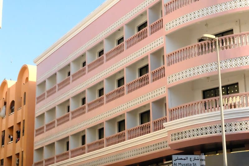 A pink and white building with multiple balconies and windows under a clear blue sky.