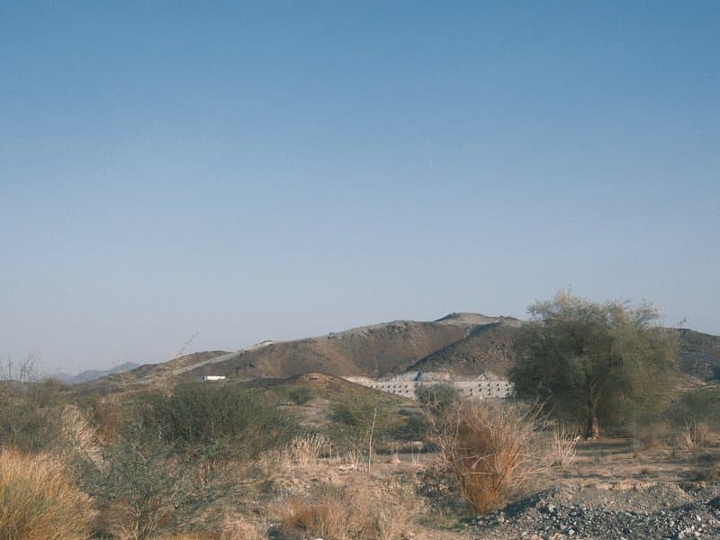 A dry landscape with rolling hills and sparse vegetation under a clear blue sky.