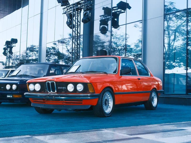 A classic red BMW car parked in front of a modern glass building with reflections.