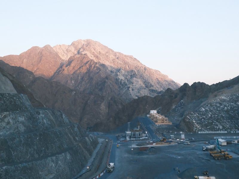 A mountainous landscape with rocky terrain and a mining site in the foreground during sunset.