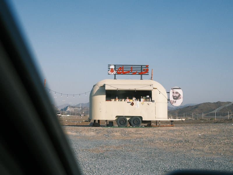 A vintage food trailer in a barren landscape with mountains in the background under a clear blue sky.