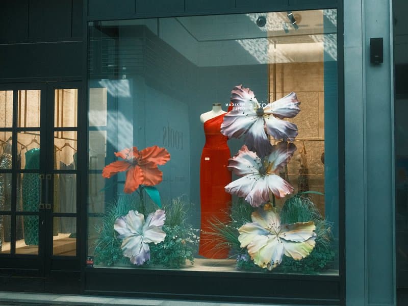 A vibrant storefront display featuring a red dress and large colorful flowers.