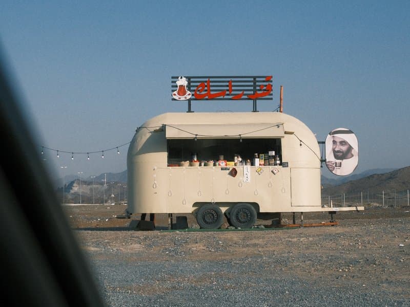 A vintage food trailer in a rural setting with a clear blue sky and mountains in the background.