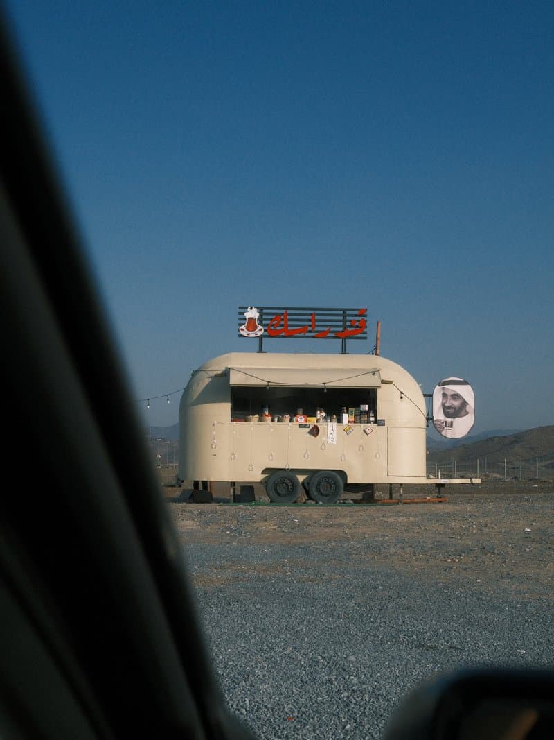 A food truck with a rounded structure set against a clear blue sky, viewed from a car window.