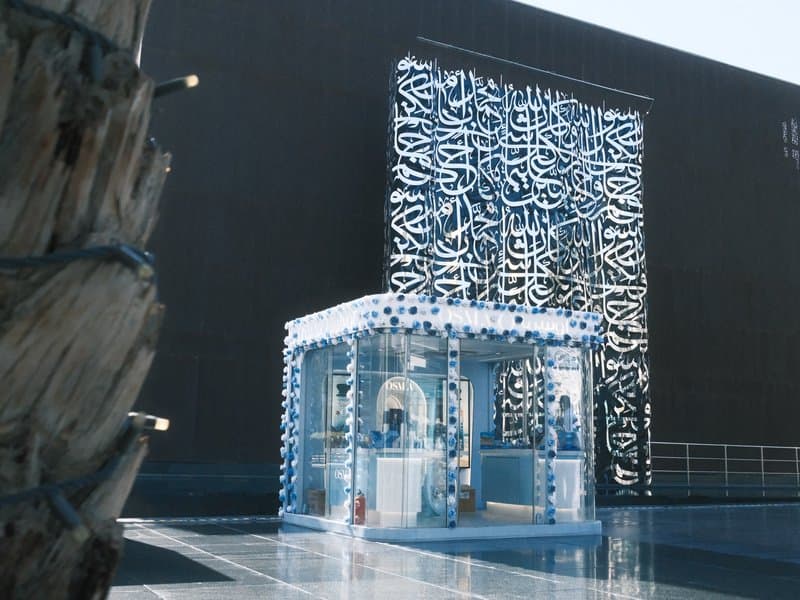Modern architectural structure with intricate patterns against a dark wall, reflecting in a shiny surface.